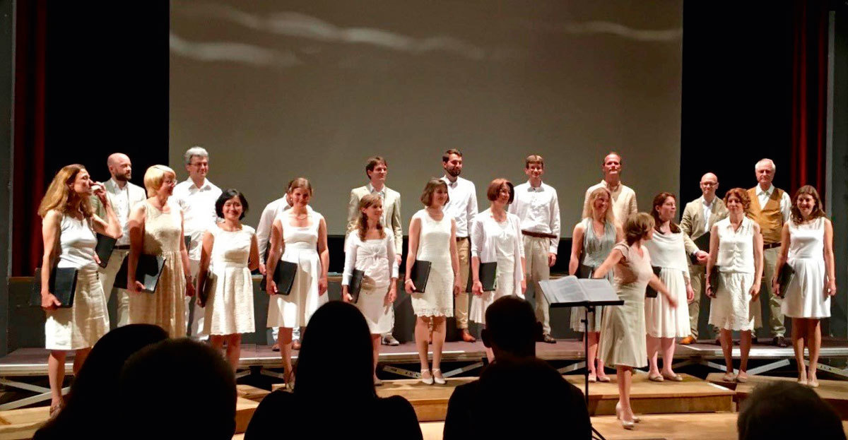 Das in Weiß gekleidete Vokal-Ensemble Canzone 11 steht auf einer Bühne, im Hintergrund ist eine Leinwand zu erkennen.