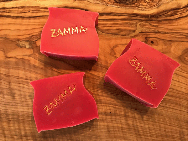 Foto mit drei ZAMMA-Sommerduftseifen,in kräftigen Rot und mit dem goldenen ZAMMA-Schriftzug.