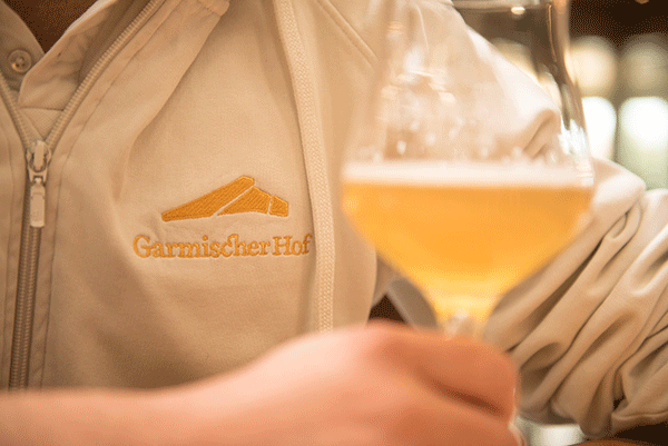 Eine Biersommeliere mit einer Jacke mit der Aufschrift "Garmischer Hof" verkostet eine helle Biersorte