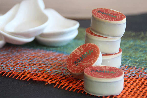 Foto von fünf ZAMMA-Pralinen, die auf einem Tisch liegen. Die ZAMMA-Pralinen sind runde weiße Törtchen mit einem roten ZAMMA-Deckel.